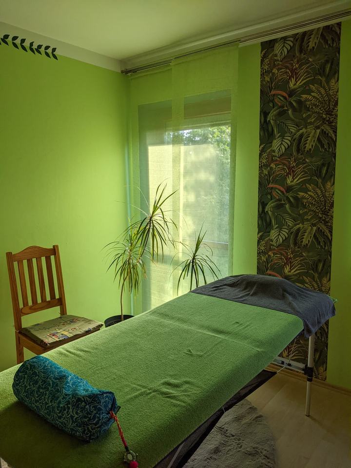 Das Massagezimmer: grüne Wände, Massageliege, Pflanze vor dem hellen Fenster
